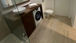 Une salle de bain moderne avec une douche à parois de verre, un lavabo avec un miroir, un lave-linge et des toilettes.