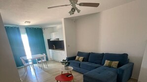 Un salon avec un canapé bleu, une table basse rouge et un ventilateur de plafond.