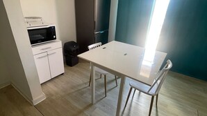 Une cuisine compacte équipée d’un four à micro-ondes, d’un réfrigérateur et de placards. On y trouve une table à manger avec deux chaises et une fenêtre avec des rideaux.