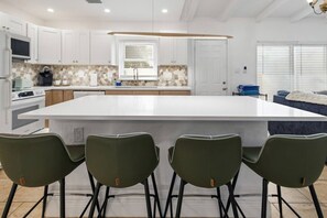 Une cuisine moderne avec des meubles blancs, un grand îlot central et un coin repas équipé de quatre chaises.