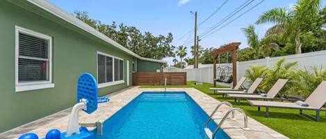 Une piscine avec un toboggan, des chaises longues et une pergola.