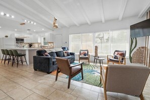 Ein modernes Wohnzimmer mit einer Couch, Sesseln, einem Couchtisch und einer Küchenzeile im Hintergrund.