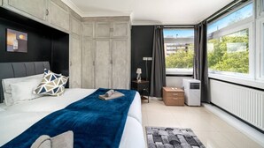 A modern bedroom with a large bed, a view of greenery outside, and a built-in wardrobe. - Stylish 2BR Flat | Oxford Street Locale (Greater London)