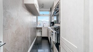 A narrow kitchen with a window, a sink, a stove, and a washing machine. - Stylish 2BR Flat | Oxford Street Locale (Greater London)