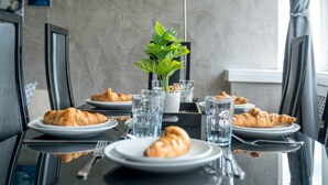 A dining table set with plates of croissants, water glasses, and a potted plant. - Stylish 2BR Flat | Oxford Street Locale (Greater London)