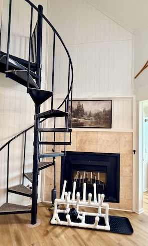 A spiral staircase with a black railing, a fireplace with a black surround, and a framed landscape painting above it.