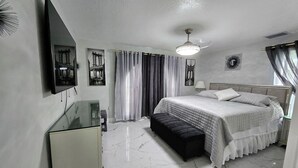 A modern bedroom with a bed, a bench, a TV, and a ceiling fan. - Beautiful 6 Room House - 10 Minutes from Disney World Parks (Kissimmee)