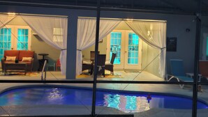 A pool area with a glass enclosure, a sofa, and a chair. - Beautiful 6 Room House - 10 Minutes from Disney World Parks (Kissimmee)