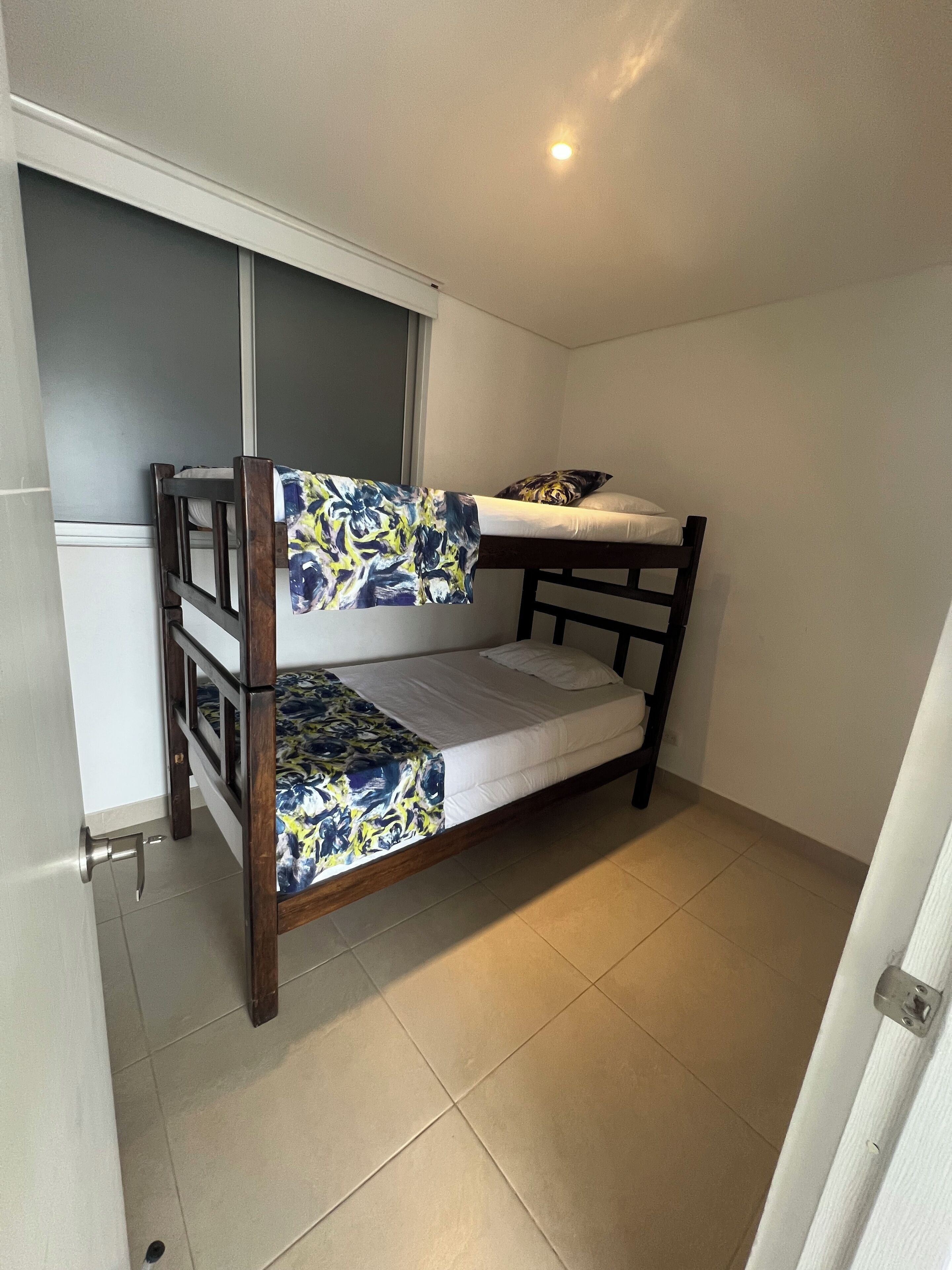 A small, compact room with a bunk bed, a small desk, and a window.