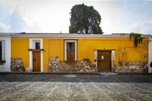 A yellow building with a stone facade, two wooden doors, and a large tree in the background.