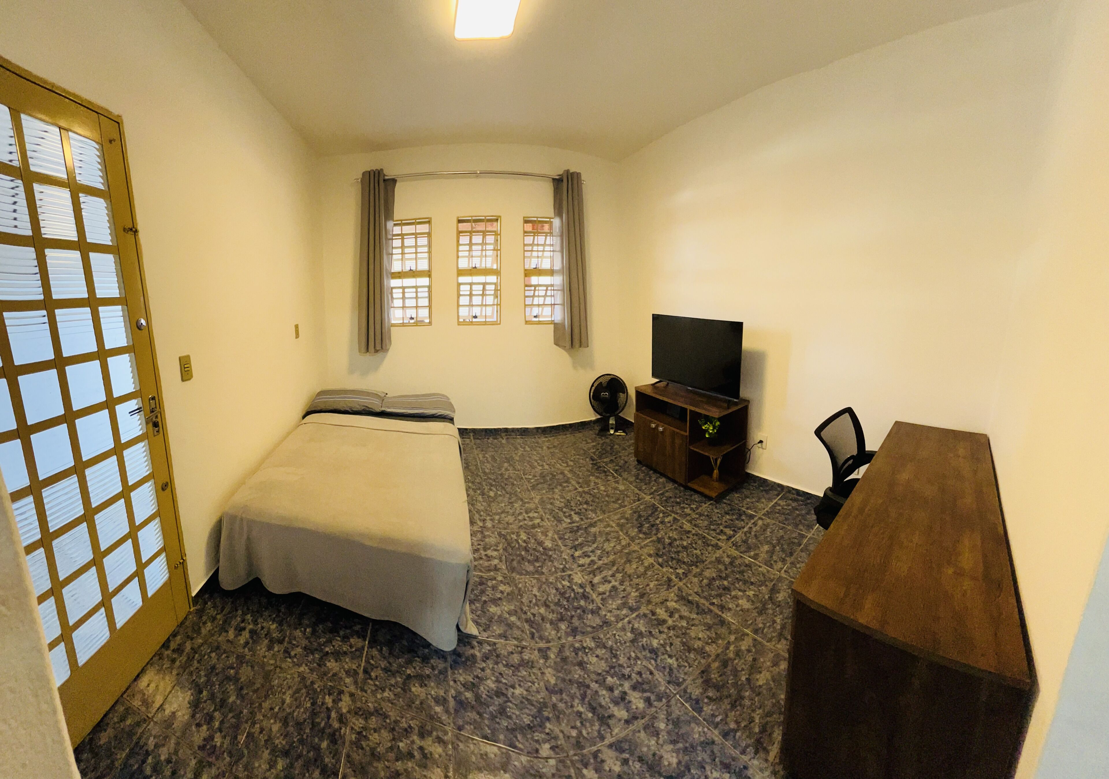 Ein Hotelzimmer mit Bett, Fernseher, Schreibtisch und einem Vorhangfenster.