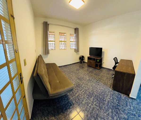 A living room with a sofa, a TV stand, and a fan.