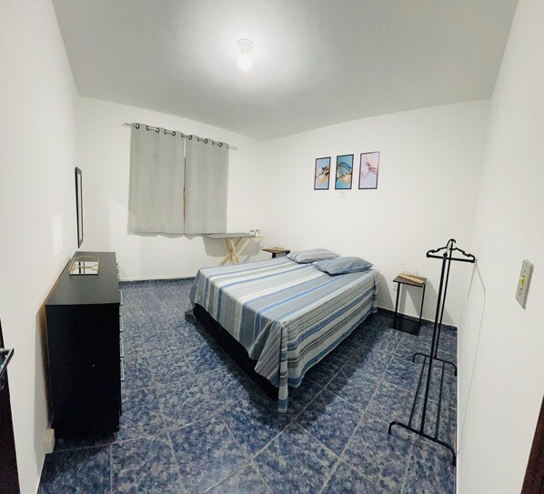 A bedroom with a bed, a desk, a chair, a coat rack, and a window with curtains.