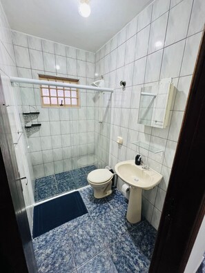 A bathroom with white tiled walls, a shower, a toilet, and a sink.