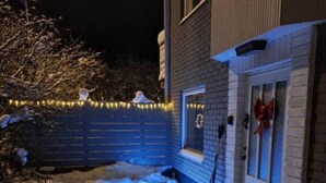 A snow-covered outdoor area with a blue fence, a white door with a red ribbon, and string lights. - Independent apartment with kitchen (Norrbottens län)