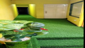 A hallway with artificial green carpet, yellow walls, and a white door at the end.