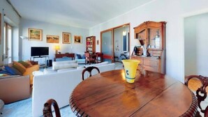 Un salón espacioso con una gran mesa redonda de madera, un conjunto de sofás y una televisión.