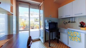 Una cocina compacta con una puerta corredera de vidrio que da a un balcón, armarios blancos y un microondas sobre una mesita.