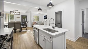A modern kitchen with a central island, pendant lighting, and a dining area with a table and chairs. - Columbus: Victorian Villa (Columbus)