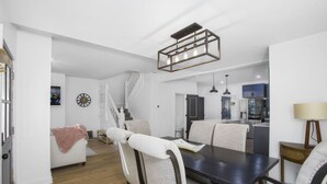 A modern dining area with a dark wooden table, white upholstered chairs, and a geometric pendant light. - Columbus: Victorian Villa (Columbus)