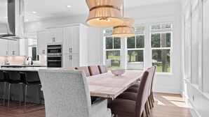 A modern kitchen with white cabinets, stainless steel appliances, and a dining area with a large table and chairs. - Lagniappe at Blue Mountain by Avantstay 4BR Coastal Home + Walk to the Beach Community Pool + Gym (Santa Rosa Beach)
