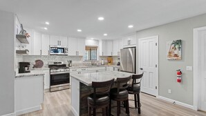 A modern kitchen with white cabinets, a central island with bar stools, stainless steel appliances, and a fire extinguisher on the wall. - 5bdr Stay w/ Fireplace, Game Room & Family-friendly Amenities Arrowhead Chalet by Avantstay (Lake Arrowhead)