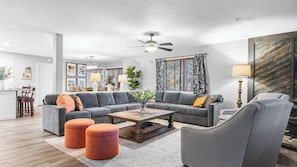 A modern living room with a grey sectional sofa, a wooden coffee table, and two orange ottomans.
