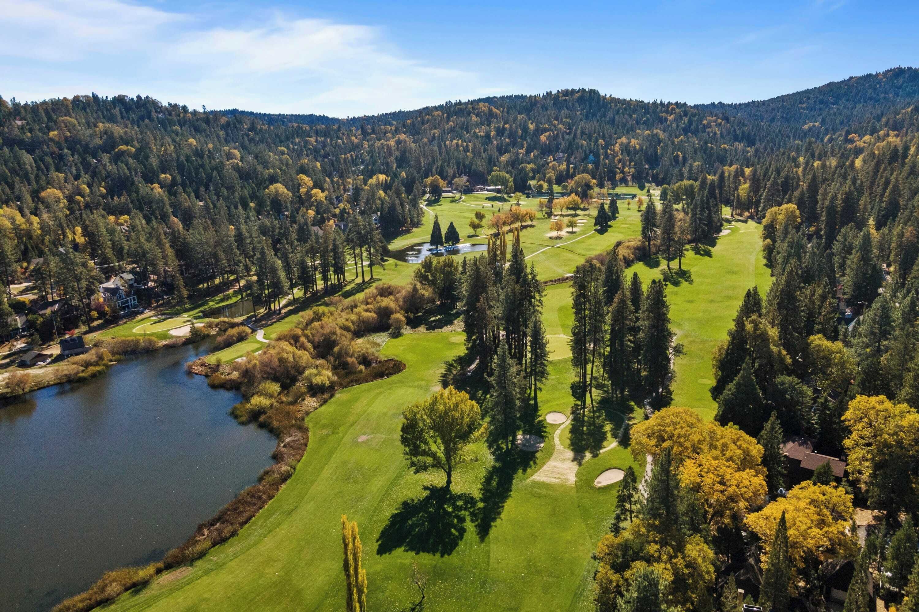 Vue aérienne d’un terrain de golf avec un lac, entouré d’une forêt dense et de collines.