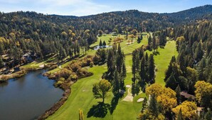 An aerial view of a golf course with a lake, surrounded by dense forest and hills. - 5bdr Stay w/ Fireplace, Game Room & Family-friendly Amenities Arrowhead Chalet by Avantstay (Lake Arrowhead)