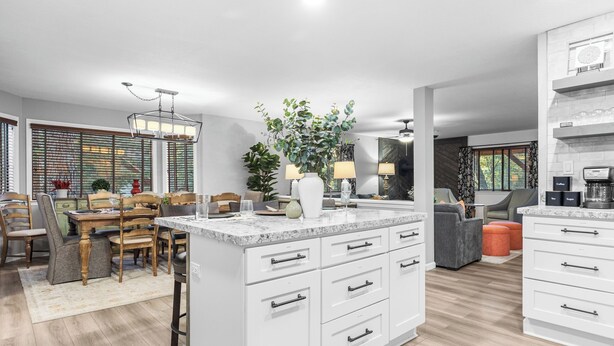 A modern kitchen with a central island, white cabinetry, and a dining area with wooden chairs. - 5bdr Stay w/ Fireplace, Game Room & Family-friendly Amenities Arrowhead Chalet by Avantstay (Lake Arrowhead)