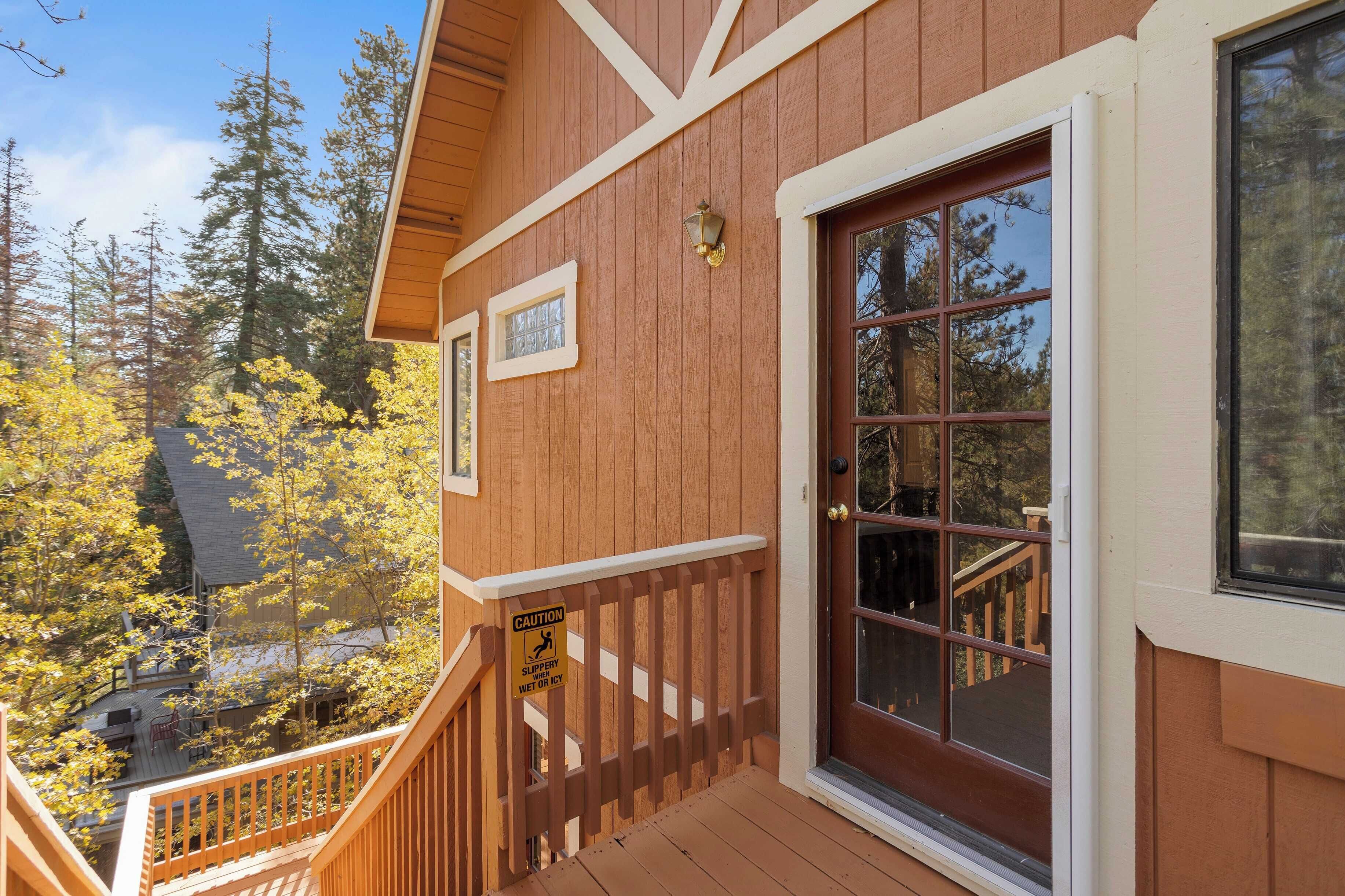 A wooden house with a deck, a glass door, and a caution sign for slippery surfaces.