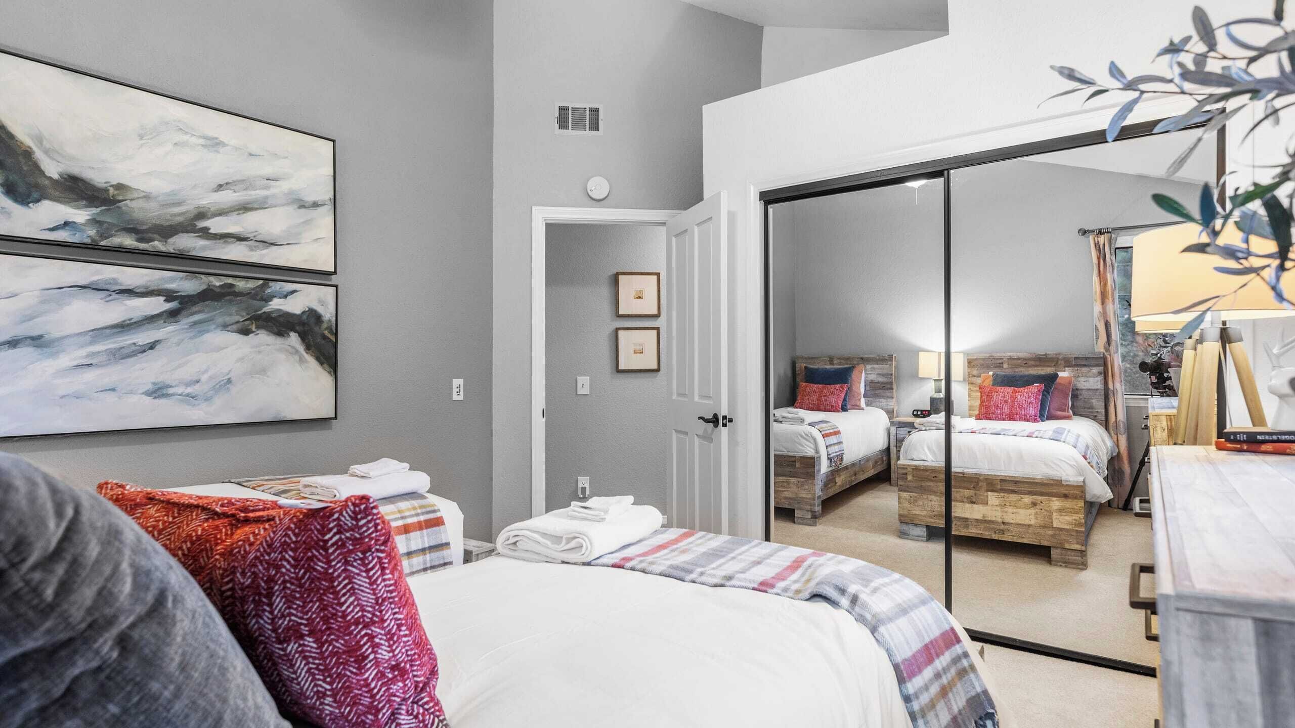 Une chambre moderne avec deux lits, un grand miroir et des œuvres d’art abstraites accrochées au mur.