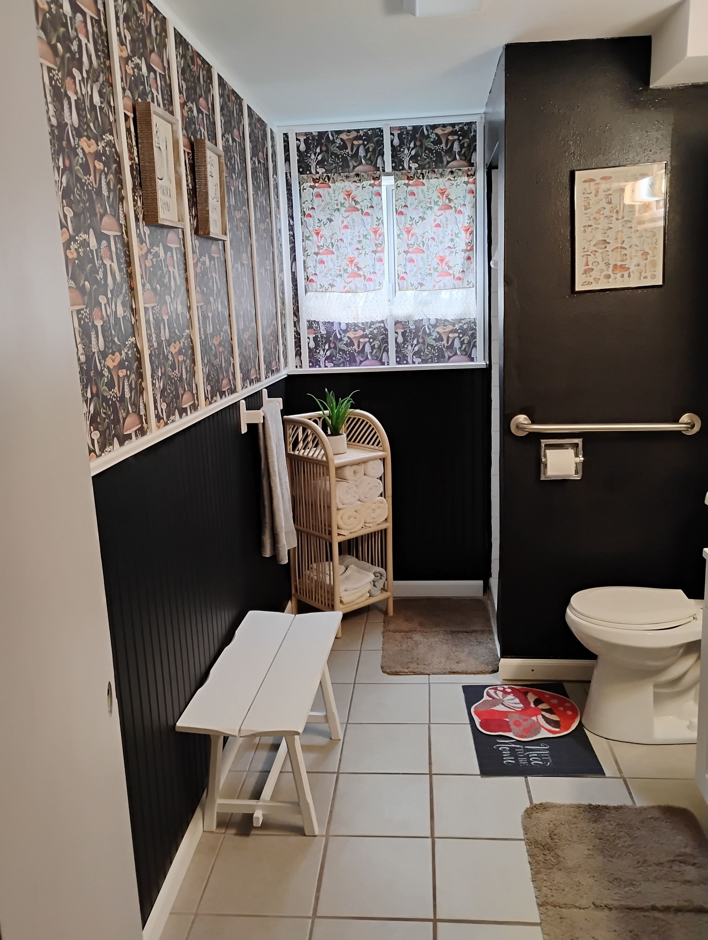 A compact bathroom with a toilet, a small bench, a shelf with towels, and a window with floral curtains.