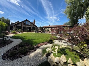 A two-story house with a patio, a lawn, and a garden with various plants and a rock feature. - Balancyoga Guesthouse (West Kingsdown)