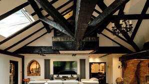 A spacious living room with a high ceiling, exposed wooden beams, a large flat-screen TV, and a fireplace. - Balancyoga Guesthouse (West Kingsdown)
