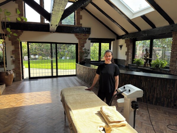 A room with a massage table, a window with a view of a garden, and a skylight. - Balancyoga Guesthouse (West Kingsdown)