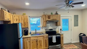 A kitchen with wooden cabinets, a black refrigerator, a stainless steel stove, and a ceiling fan. - Charming 1-bedroom cottage in Covington with AC (Covington)