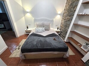 Ein Schlafzimmer mit Bett, Nachttischen, einer Steinwand und einem Holzboden.