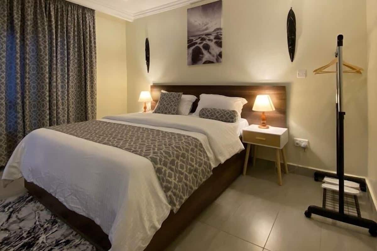 A hotel room with a large bed, two bedside tables with lamps, a wall-mounted artwork, and a floor lamp.