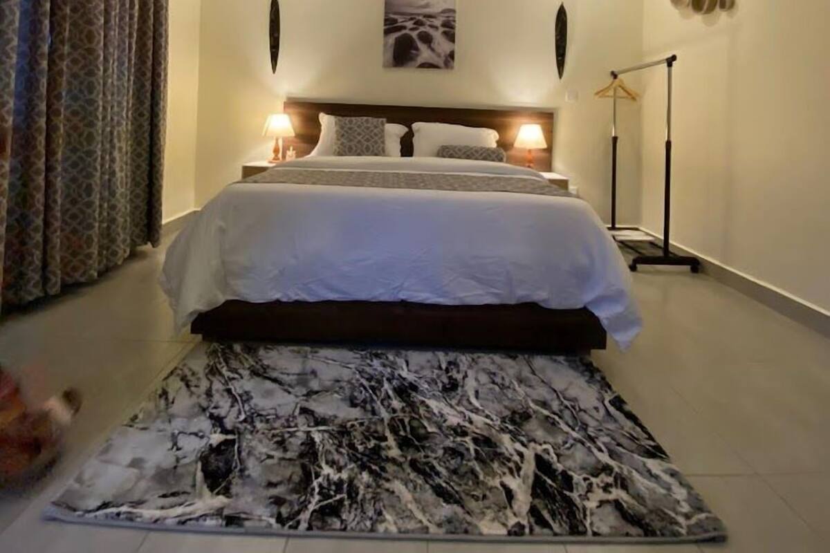 A bedroom with a bed, a headboard, a painting, a floor lamp, and a patterned rug.