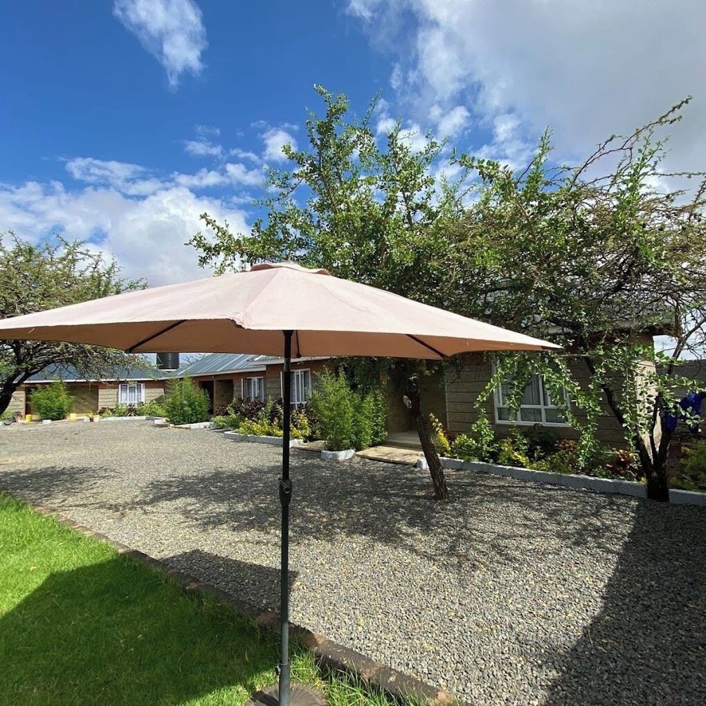 A patio area with a beige umbrella, gravel ground, and a house in the background.