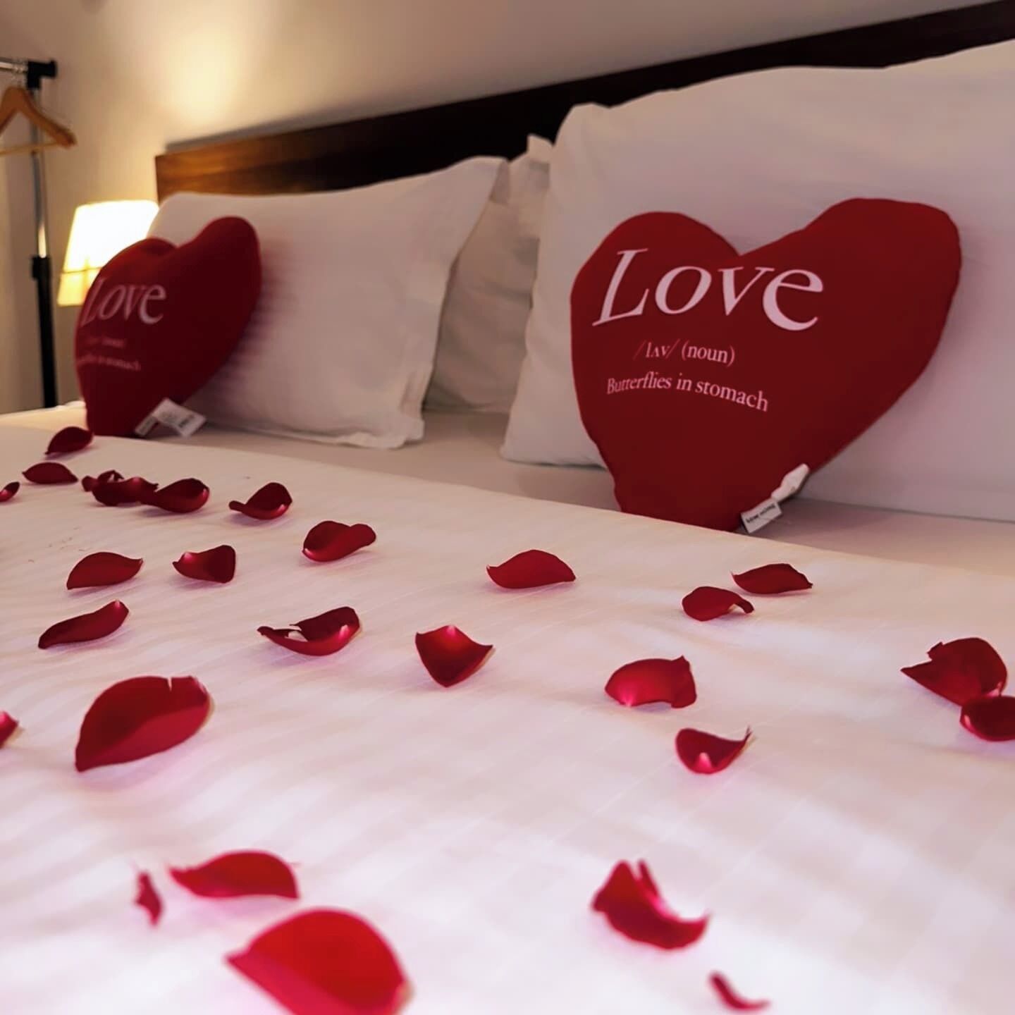 Una cama con almohadas con forma de corazón y pétalos de rosa esparcidos.