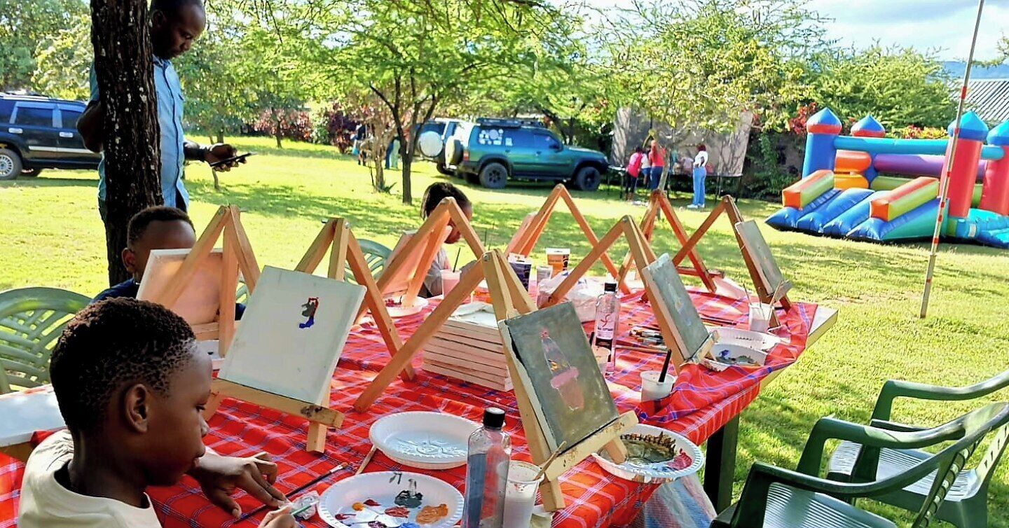Actividad artística al aire libre con caballetes y materiales de pintura sobre un mantel a cuadros.