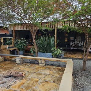 A stone patio with a fire pit, surrounded by potted plants and a wooden bench. - Tala Cottages (Nguluni)