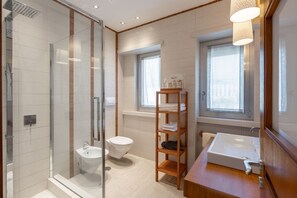 A modern bathroom with a glass shower enclosure, a white sink, and a wooden shelf with toiletries.