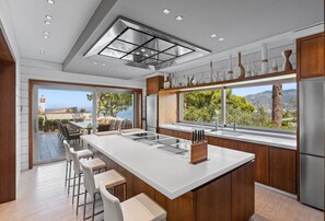 A modern kitchen with a large island, bar stools, a built-in oven, and a view of the outdoors. - Luxury Villa with pool, gym & garden in Sorrento (Priora)