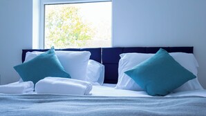 A neatly made bed with white linens and teal pillows, a dark headboard, and a window with a view of trees. - 5BR House | Free Parking | Fast Wi-Fi | Sleeps 10 (Wolverhampton)