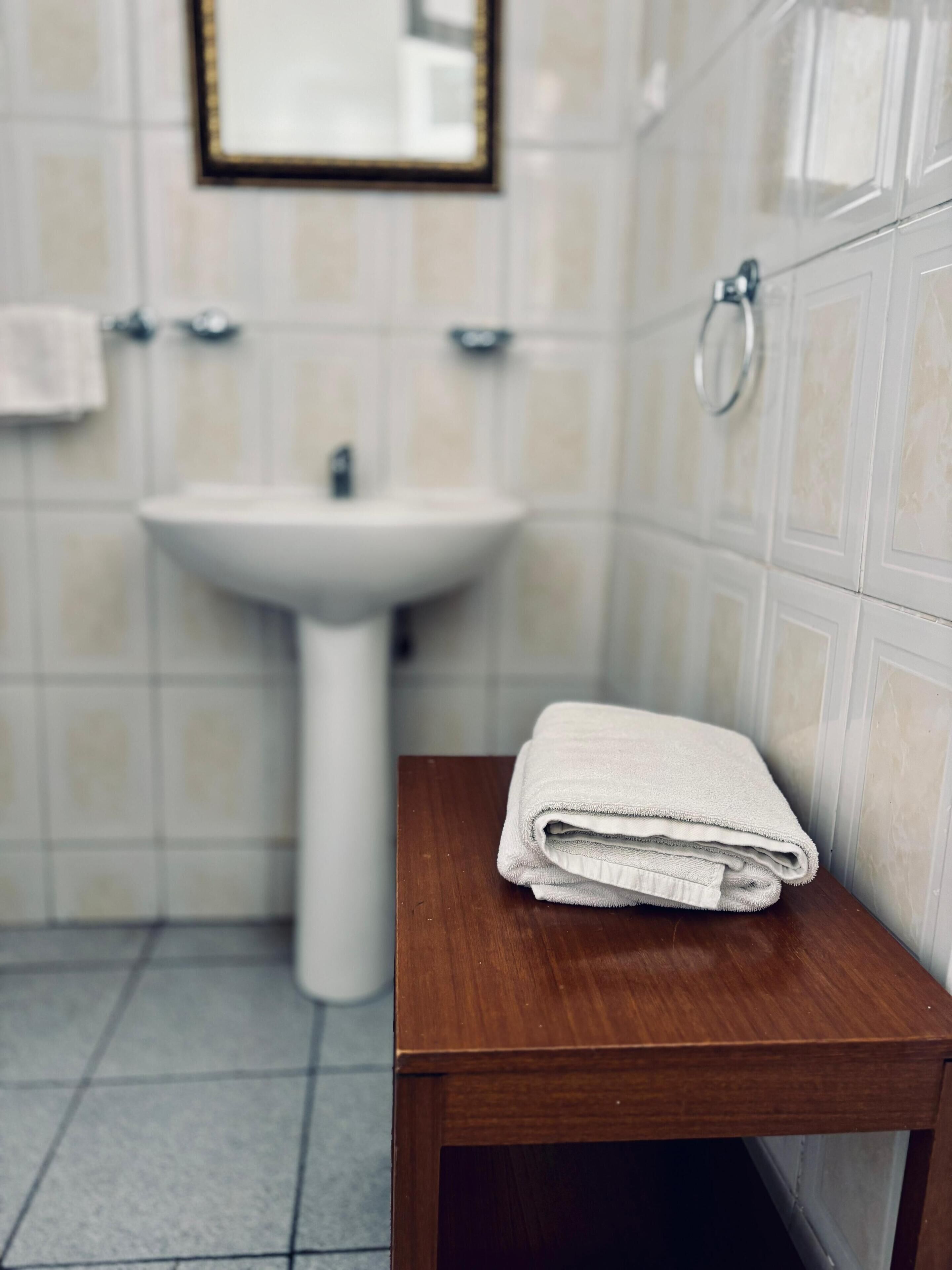 A bathroom with a sink, a mirror, and a wooden table with a folded towel.