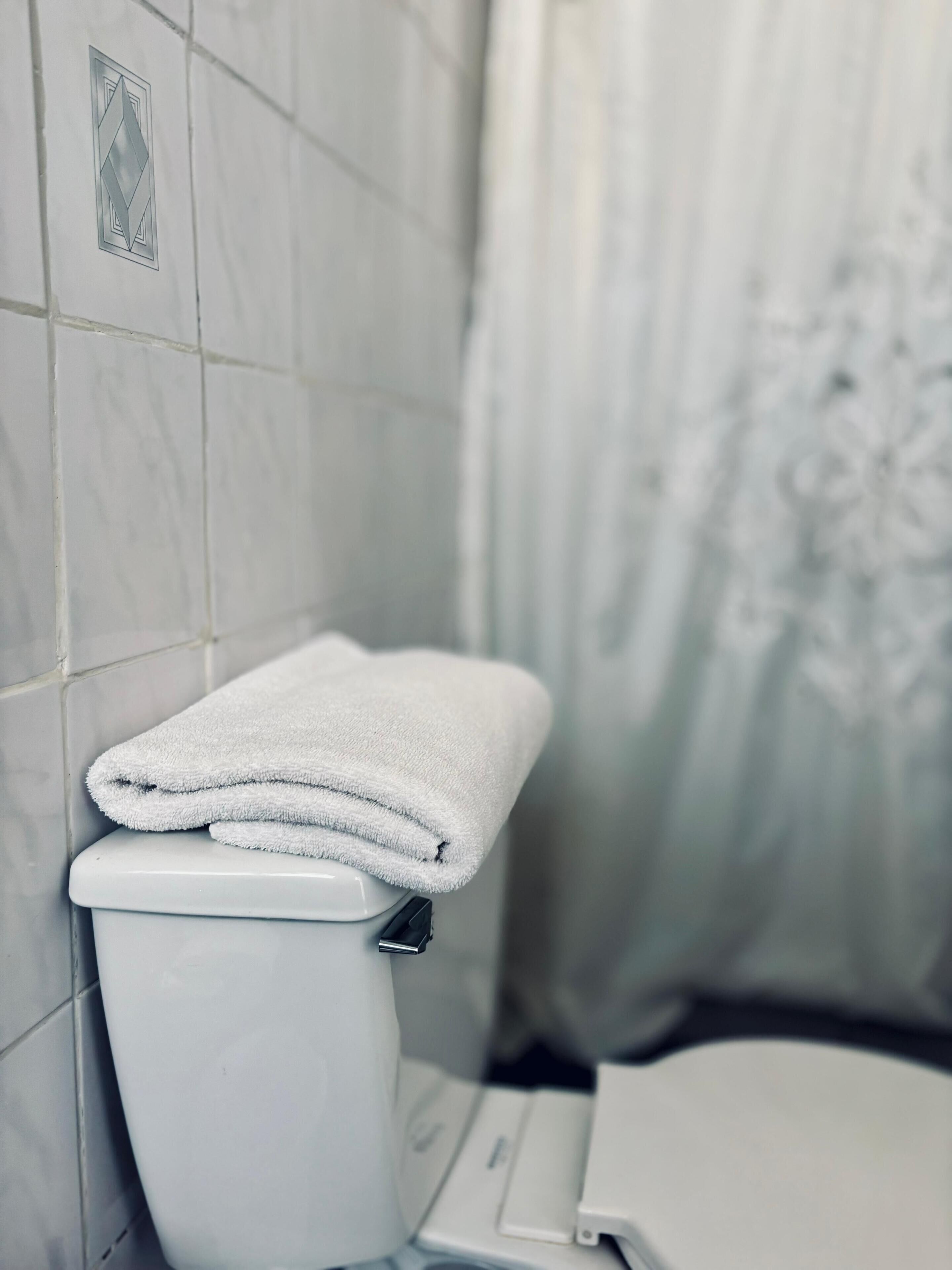 Un baño con un inodoro blanco, una toalla sobre el tanque y una cortina de ducha.