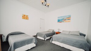 Una habitación con dos camas individuales, una mesita de noche, una lámpara y dos cuadros en las paredes.